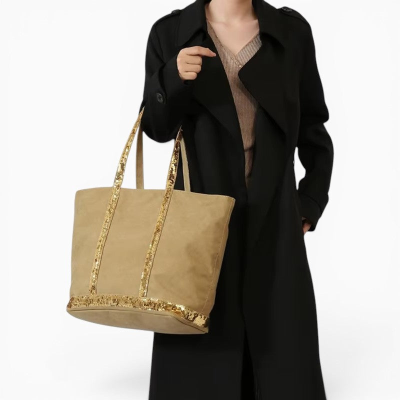 Sac grand cabas beige en toile avec détails à paillettes dorées porté à l'épaule par une femme en manteau noir