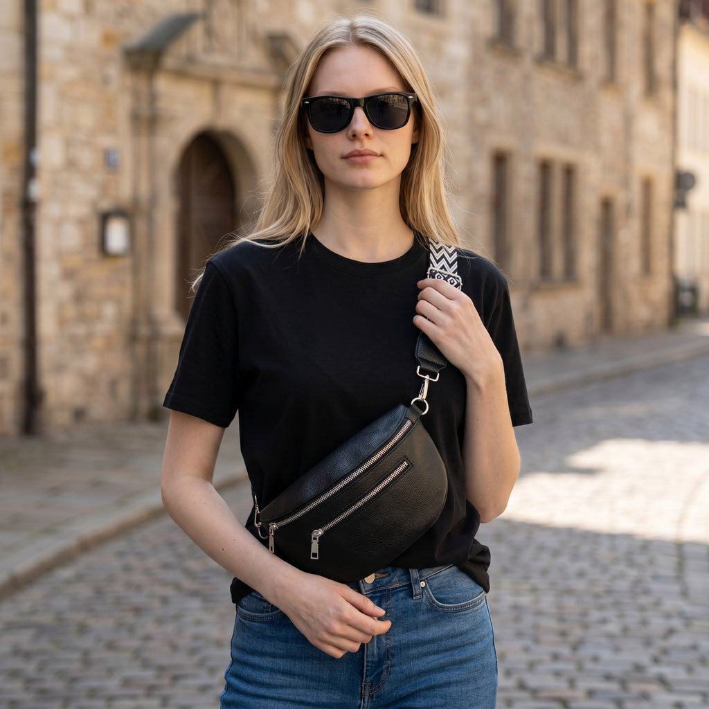 Femme portant un sac banane noir en cuir souple Sac avec bandoulière large à motifs dans une rue pavée