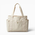 Sac fourre-tout en toile beige de la marque Sac, style preppy avec poches extérieures et fermeture zippée.